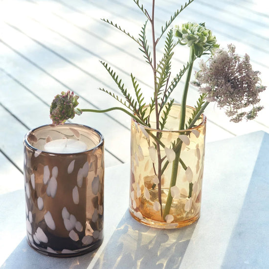 Two glass containers with candles and plants on a light surface