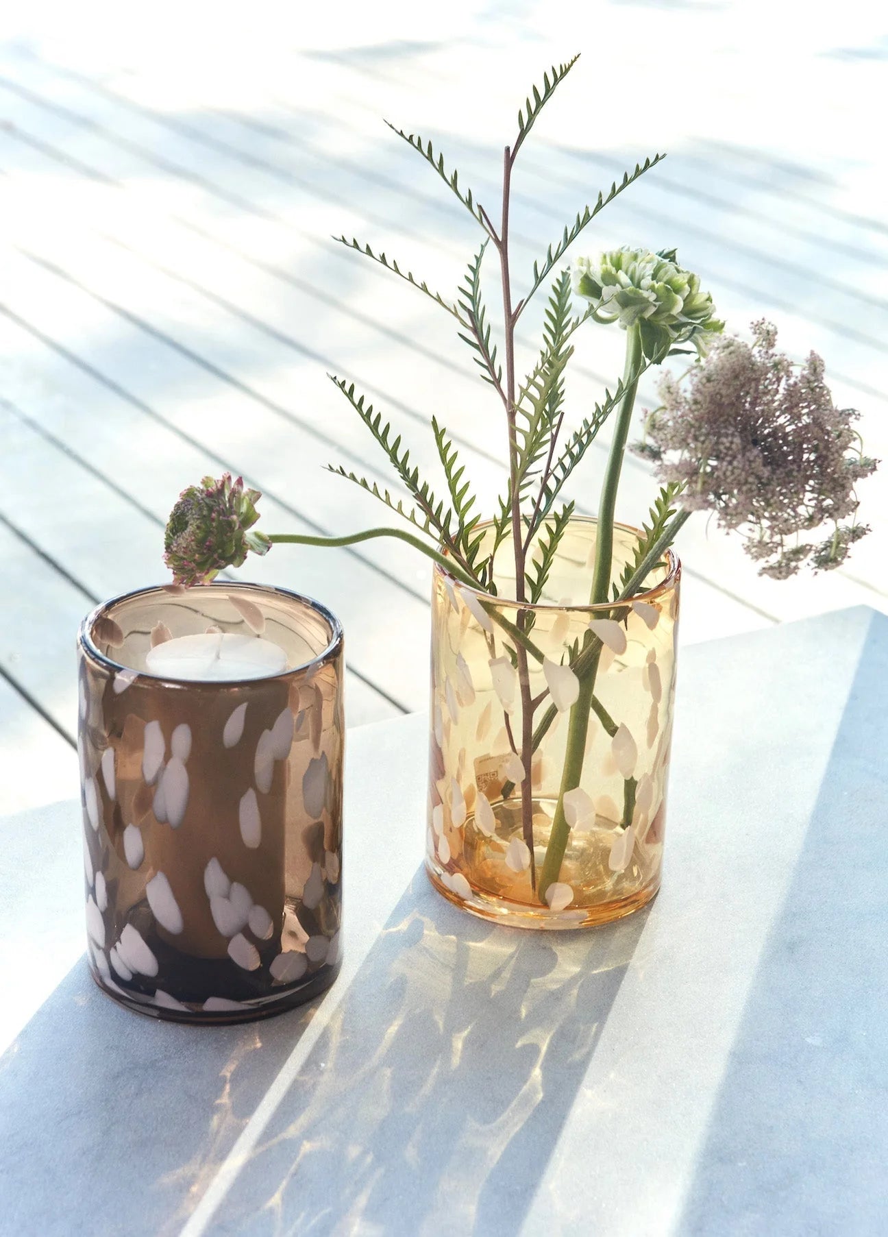 Two glass containers with candles and plants on a light surface
