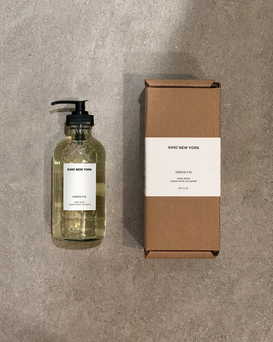 Glass bottle with pump and cardboard box labeled 'Kiho New York' on a gray concrete surface