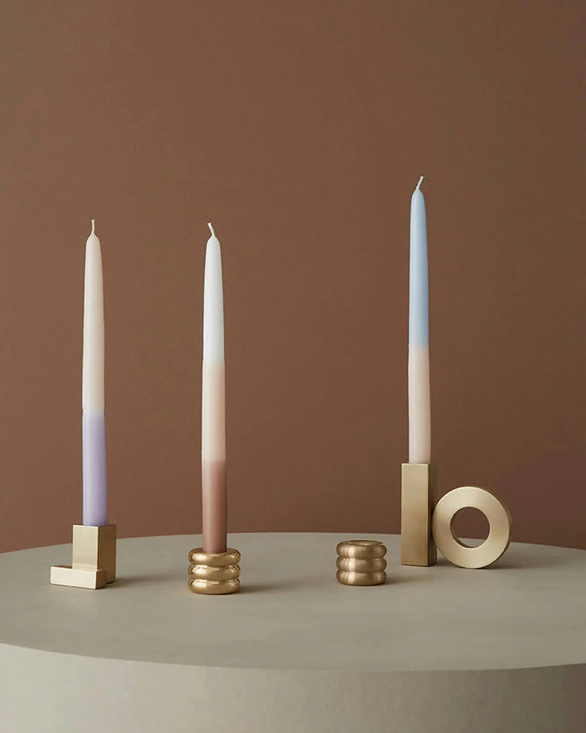 Three candles with gradient colors in holders on a neutral background