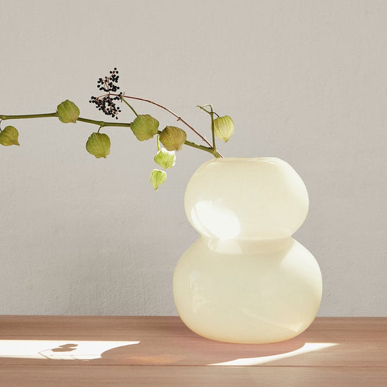 Modern vase with a branch on a wooden surface against a plain wall