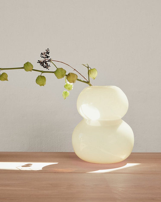 Modern vase with a branch on a wooden surface against a plain wall