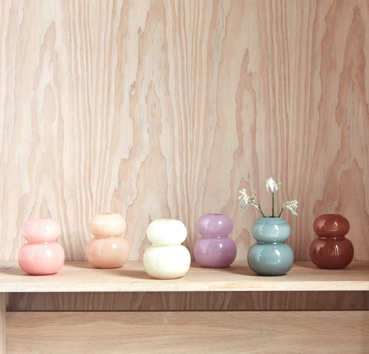 Three ceramic vases in pastel colors on a wooden surface with a light wood grain background