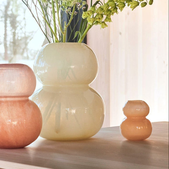Three glass vases on a wooden cabinet with a window in the background