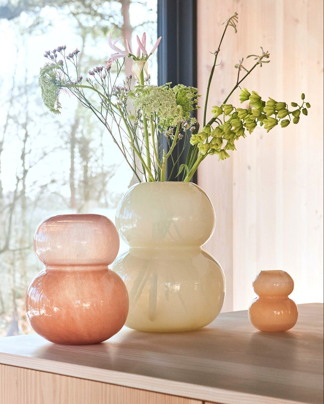 Three glass vases on a wooden cabinet with a window in the background