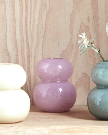 Three ceramic vases of different colors on a wooden surface with a light wood panel background.