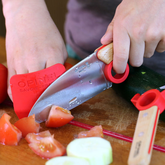 Child using a children's knife set to cut vegetables on a wooden cutting board.