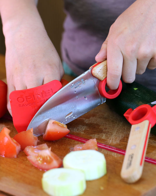 Child using a children's knife set to cut vegetables on a wooden cutting board.