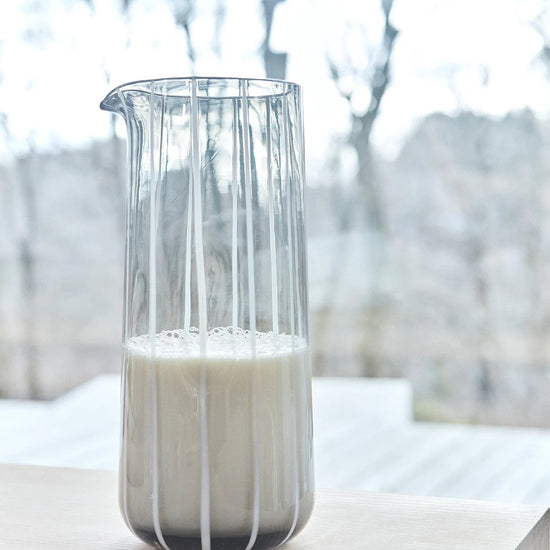 Gray glass carafe filled with milk on a light surface with a blurred natural background