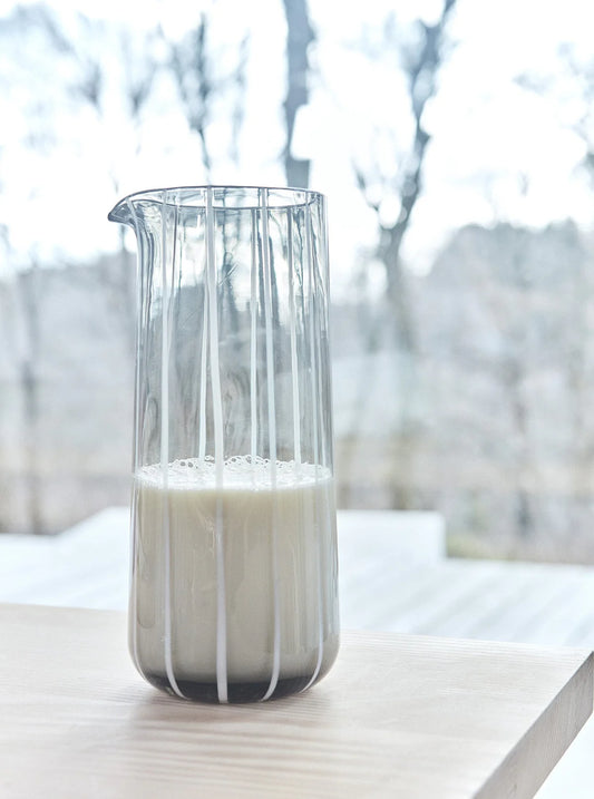 Gray glass carafe filled with milk on a light surface with a blurred natural background