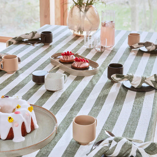 Dining table setting with striped tablecloth, cups, plates, and decorative items.