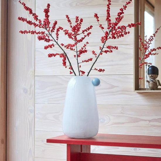 White vase with red branches on a red bench against a wooden wall.