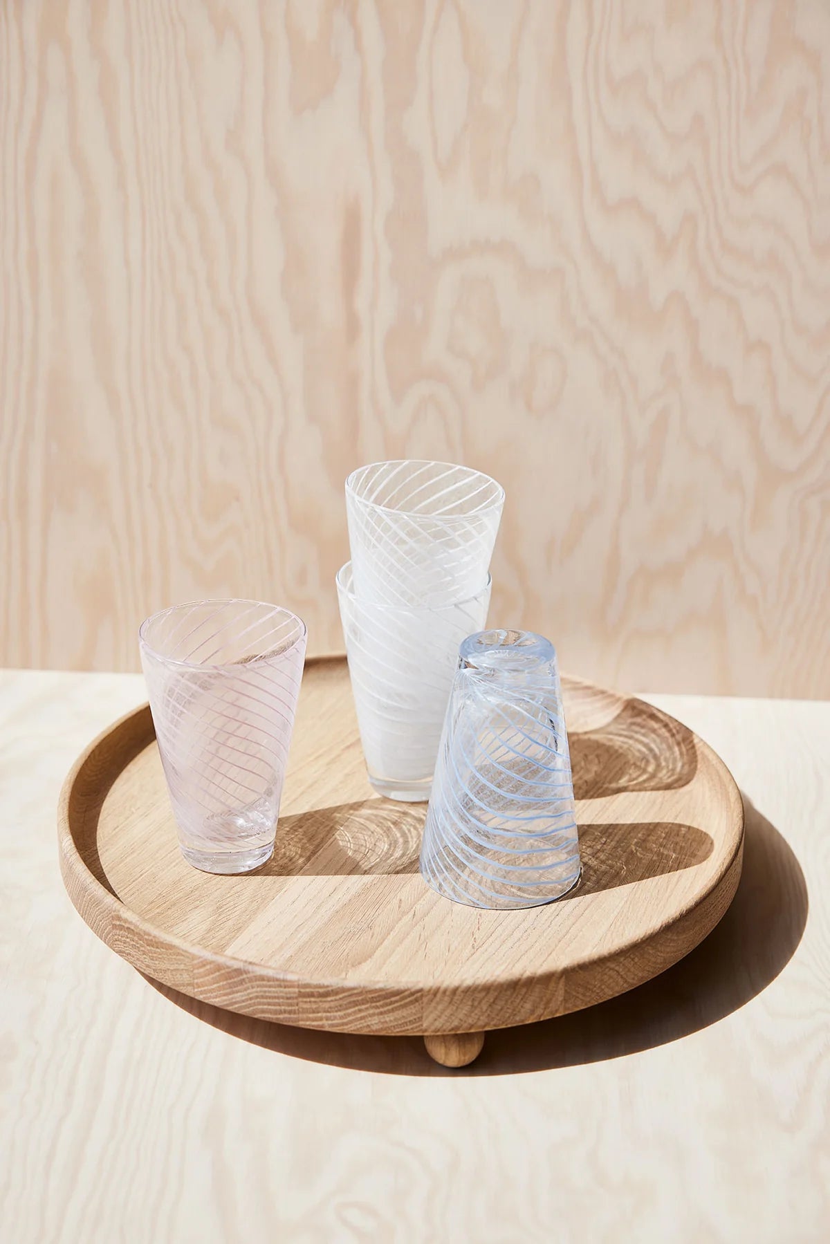 Three glass tumblers on a wooden tray against a light wood panel background
