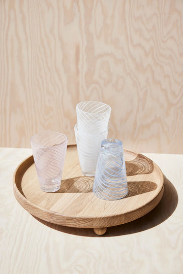 Three glass tumblers on a wooden tray against a light wood panel background