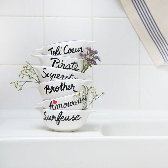 Set of white bowls with black text and floral designs on a kitchen counter.