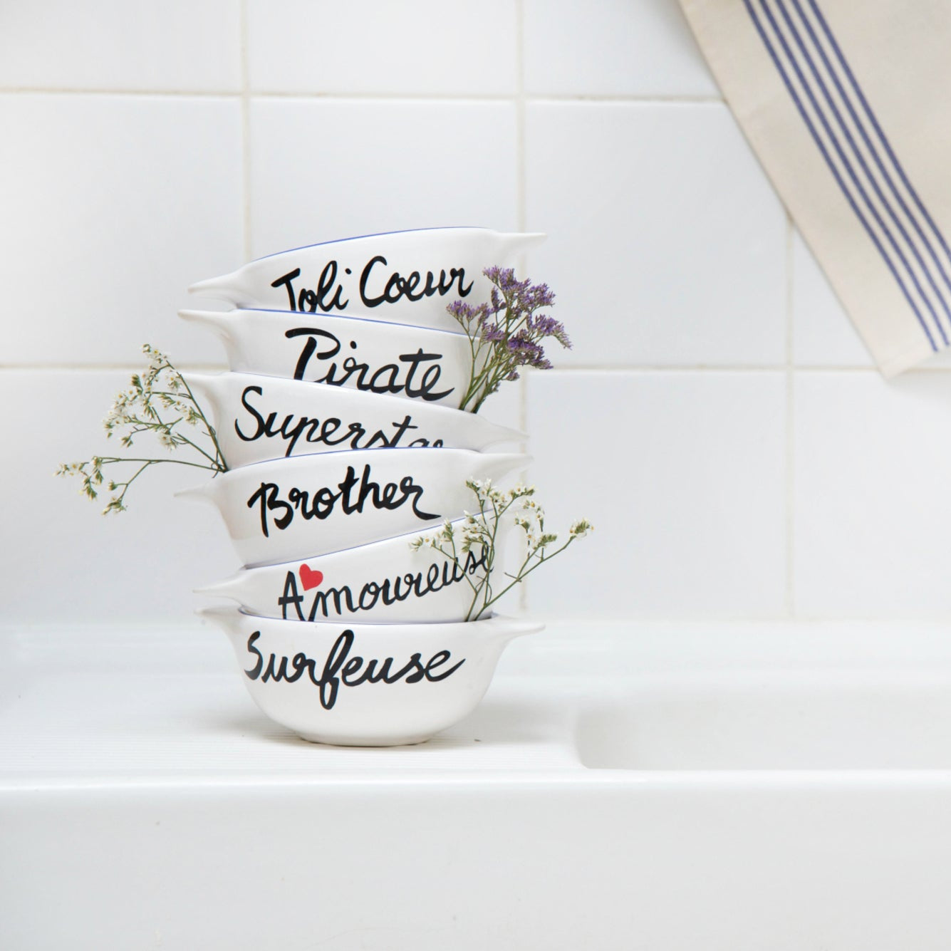 Set of white bowls with black text and floral designs on a kitchen counter.