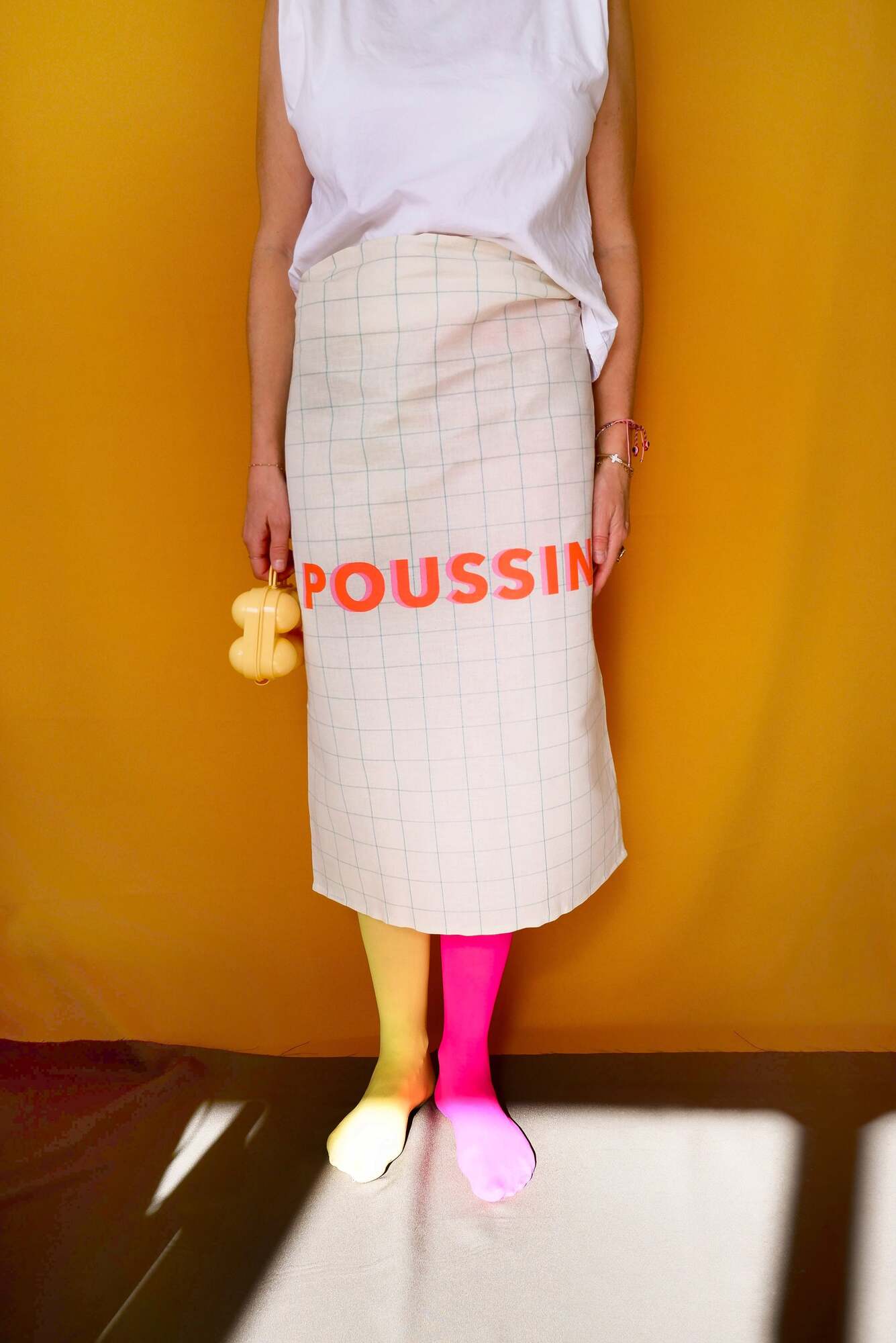 Person wearing a white apron with 'POUSSIN' printed on it against a mustard yellow background.