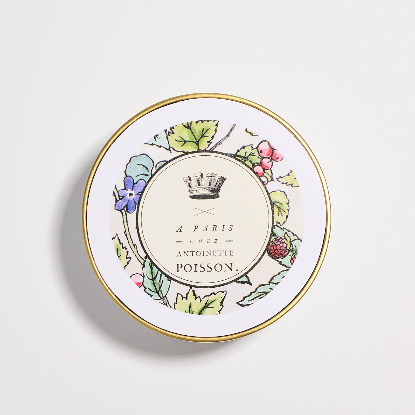 Top view of a jar lid with a gold rim and a floral design surrounding the text “A Paris Chez Antoinette Poisson”