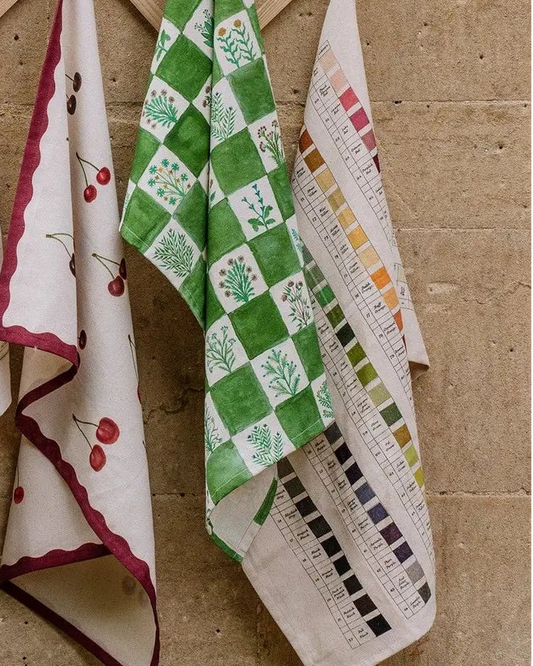 Set of patterned kitchen towels hanging on a wooden rack against a beige wall.