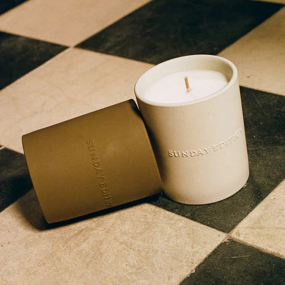 Candle and packaging on a checkered floor with 'SUNDAY' branding.