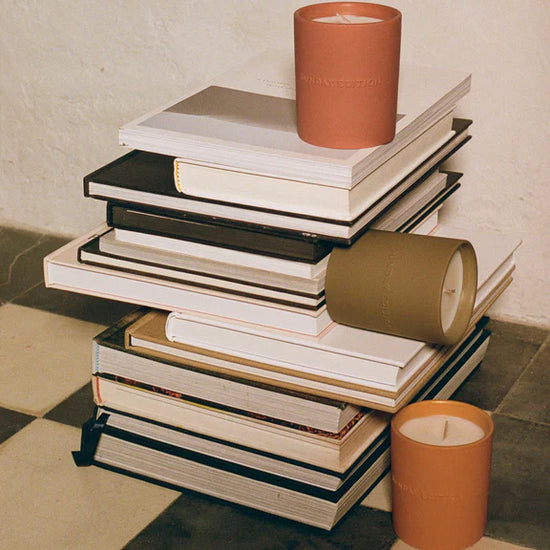 Stack of books with a candle on top, placed on a checkered floor.