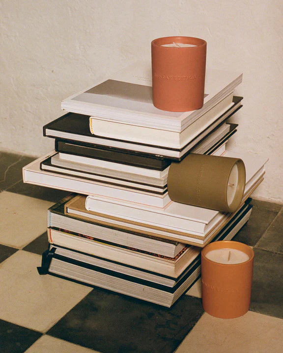 Stack of books with a candle on top, placed on a checkered floor.