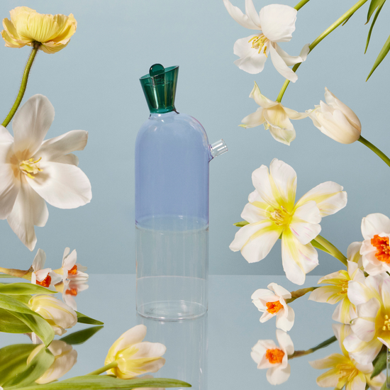 Clear bottle with green cap surrounded by white and yellow flowers on a light blue background