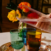 Person pouring a water into three glass cups with flowers on a tray.