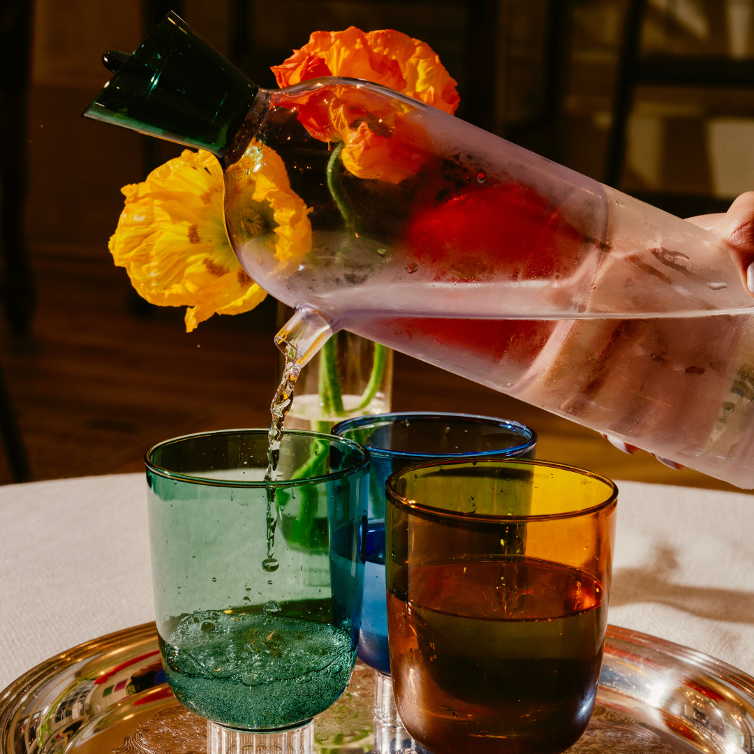 Person pouring a water into three glass cups with flowers on a tray.