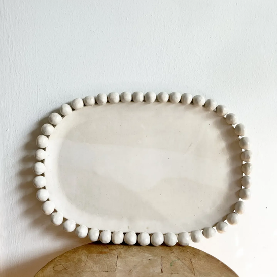 White ceramic platter with decorative edge on a wooden surface against a white wall