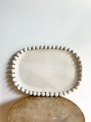 White ceramic platter with decorative edge on a wooden surface against a white wall