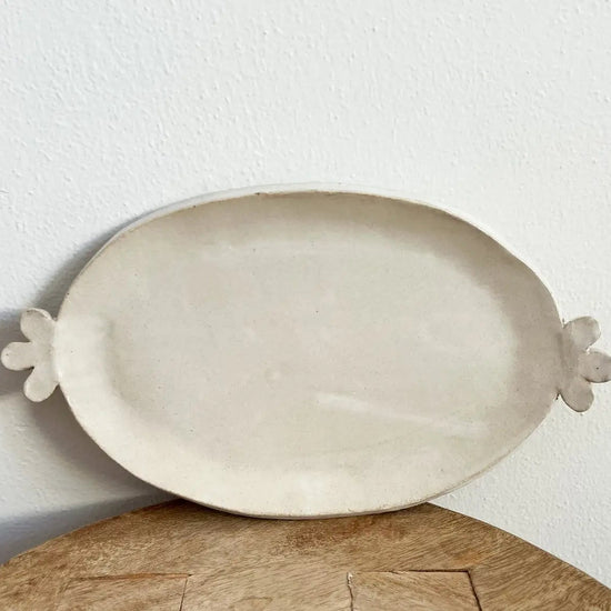 White ceramic platter with floral handles on a wooden surface