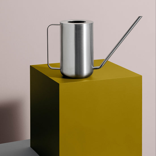 Silver watering can on a green cube against a plain background