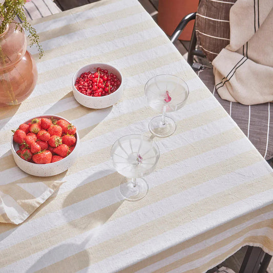 Outdoor table setting with strawberries, cherries, and glasses on a yellow striped tablecloth.