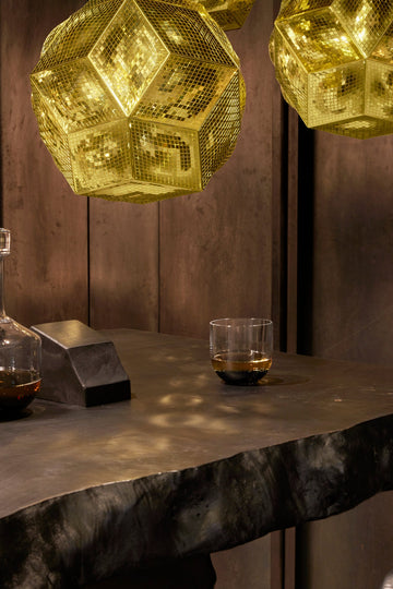 Three geometric pendant lights hanging above a dark wooden table with a glass of whiskey.
