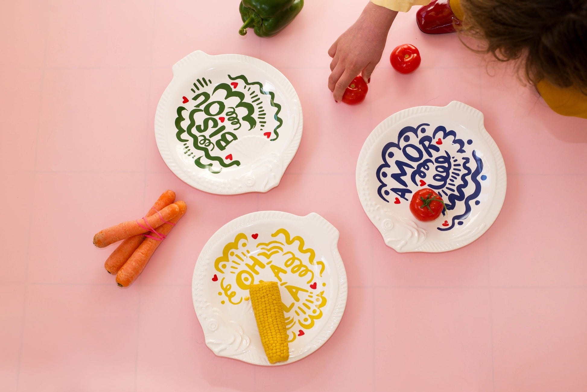 Three white plates with colorful designs and vegetables on a pink background