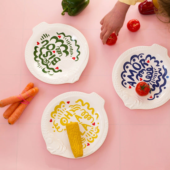 Three white plates with colorful designs and vegetables on a pink background