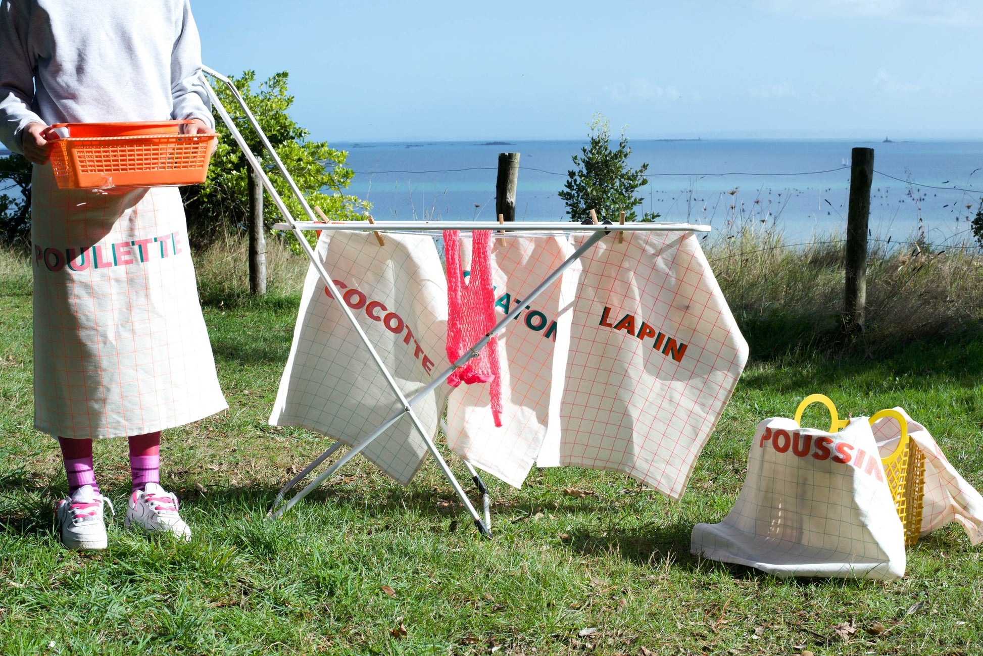 Person with laundry basket near a clothesline with hanging laundry by the sea.