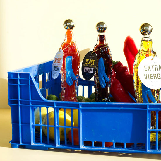 Blue crate with bottles of olive oil and vegetables on a light background