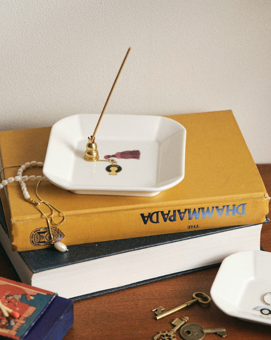 Incense stick on a white dish with books and keys in the background