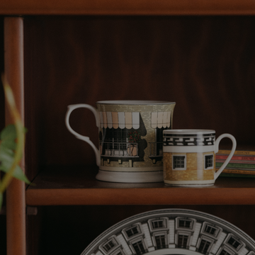 Two ceramic cups with architectural designs on a wooden shelf.