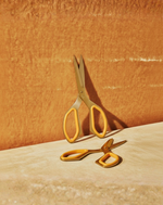 Gold scissors on a textured orange surface