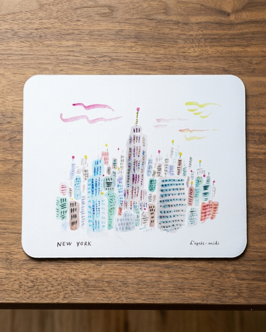 Colorful illustration of New York cityscape on a white mouse pad, placed on a wooden surface.