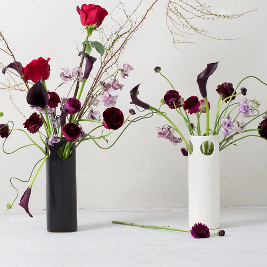 Two flower arrangements in black and white vases on a white surface with a white background