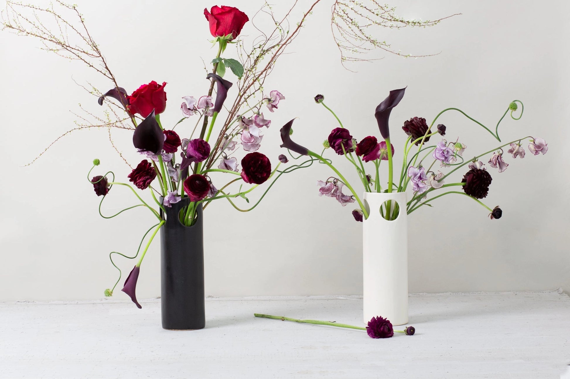 Two flower arrangements in black and white vases on a white surface with a white background
