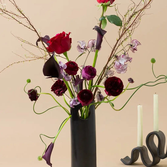 Floral arrangement with red and purple flowers in a black vase on a beige background