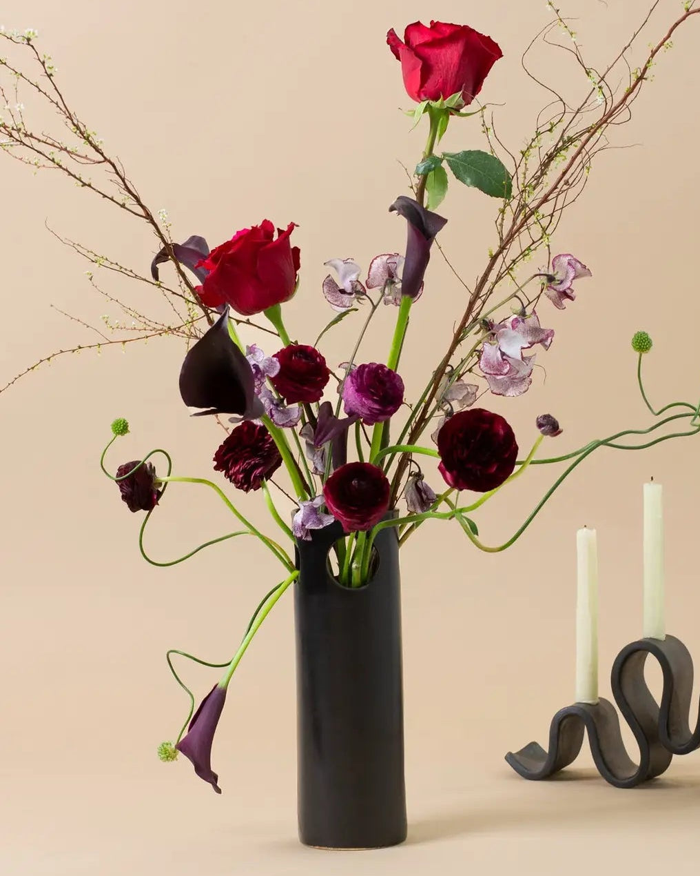 Floral arrangement with red and purple flowers in a black vase on a beige background