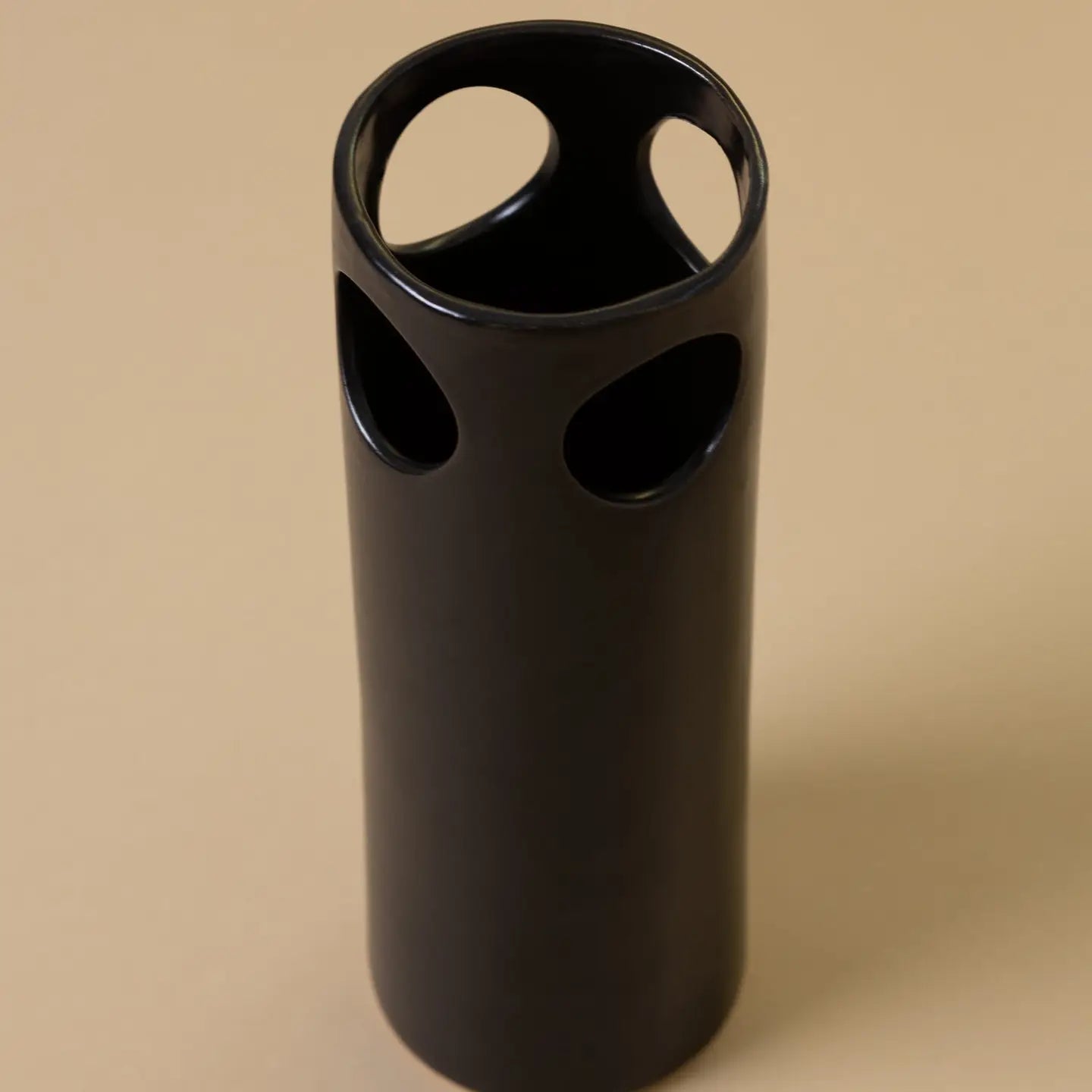 Black cylindrical vase with circular holes on a beige background