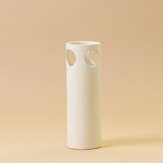 White ceramic vase with circular cutouts on a beige background