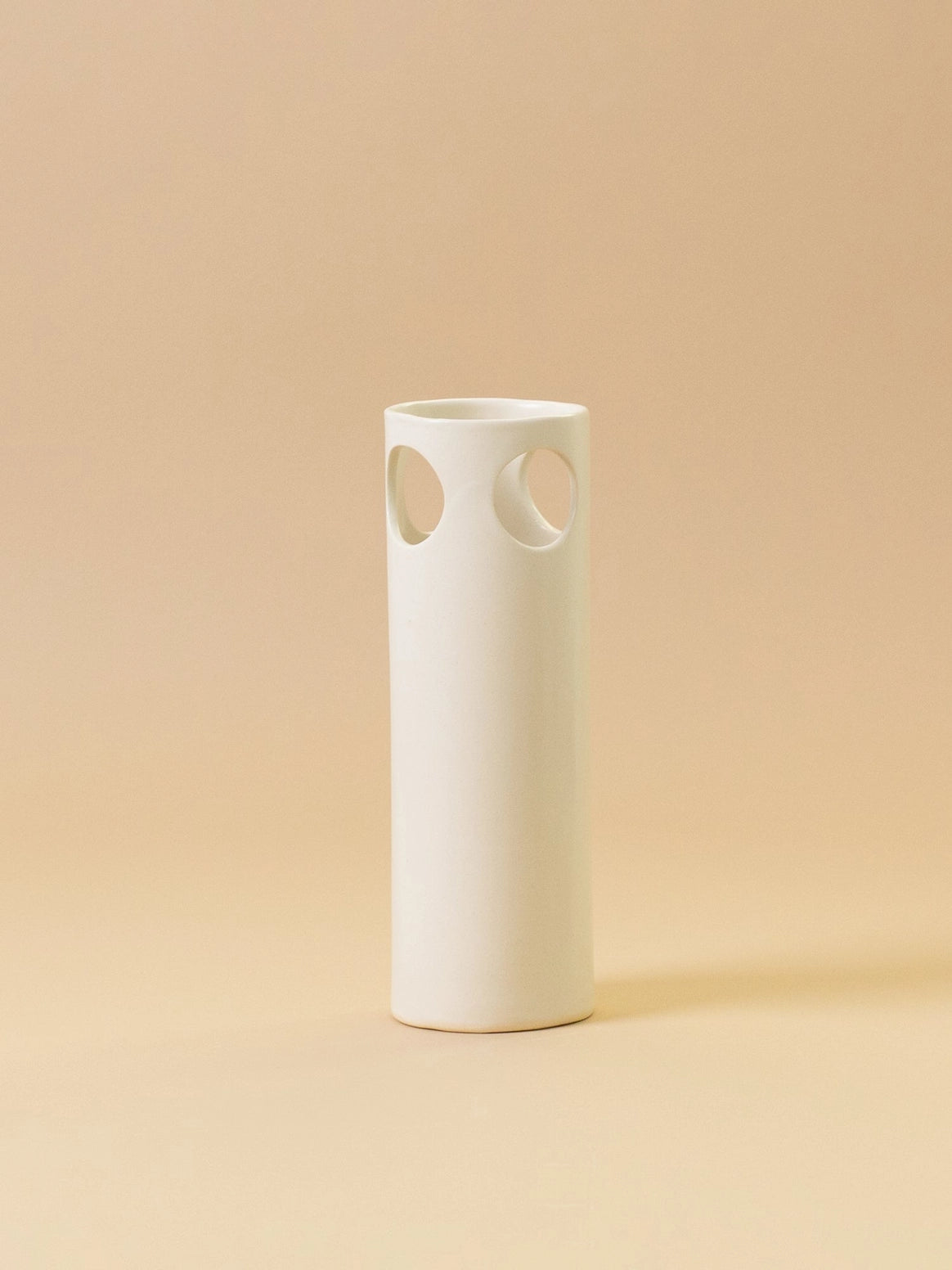 White ceramic vase with circular cutouts on a beige background